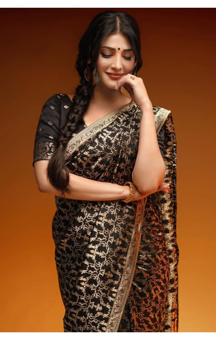 Woman wearing a black Banarasi silk saree with gold zari weaving and traditional gold border, styled with a black blouse, posing elegantly.