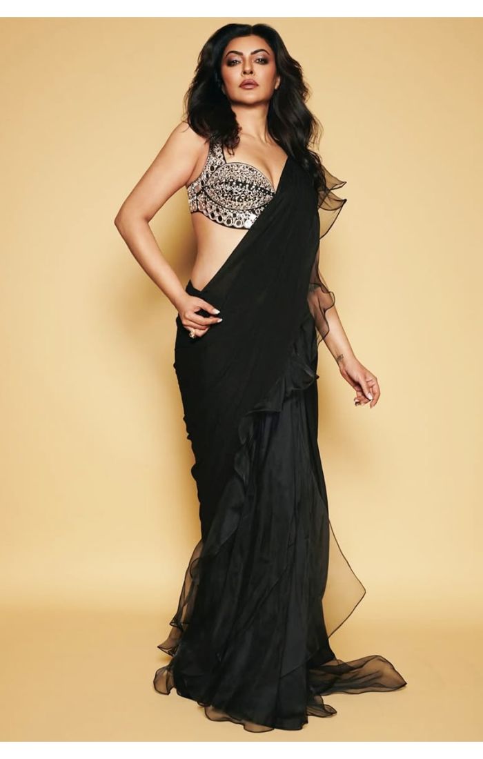 Model in black ruffle georgette saree posing with soft curls and sequin mirror blouse.