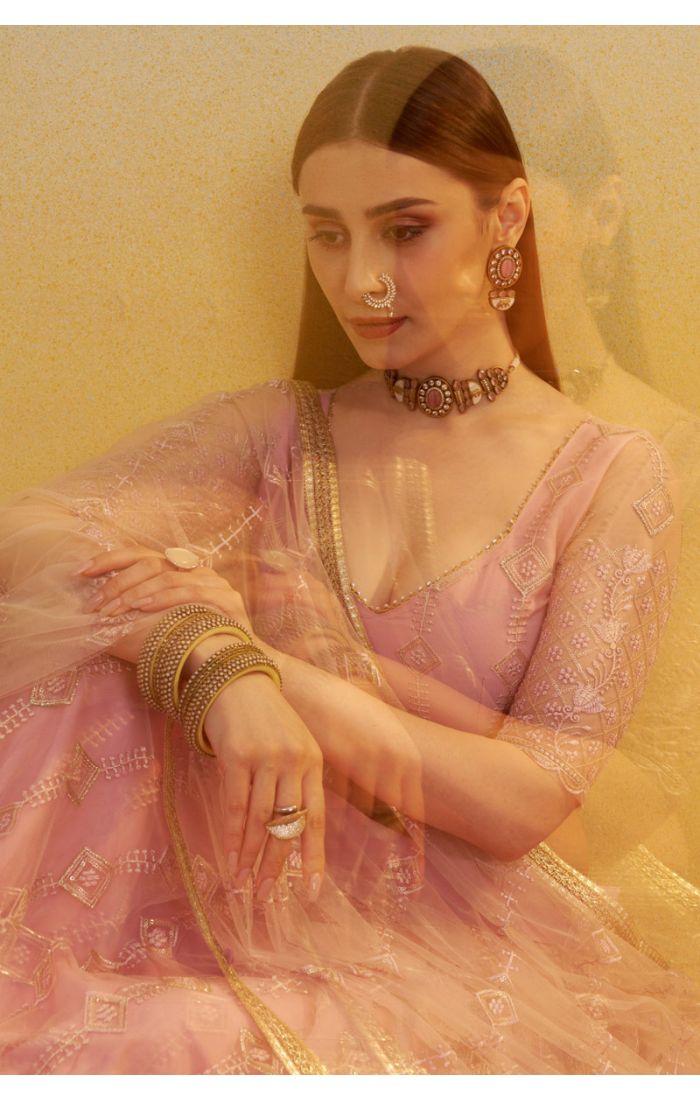 Detailed shot of blush pink net lehenga blouse and sheer dupatta with intricate embroidery and sequins, luxury ethnic wear.